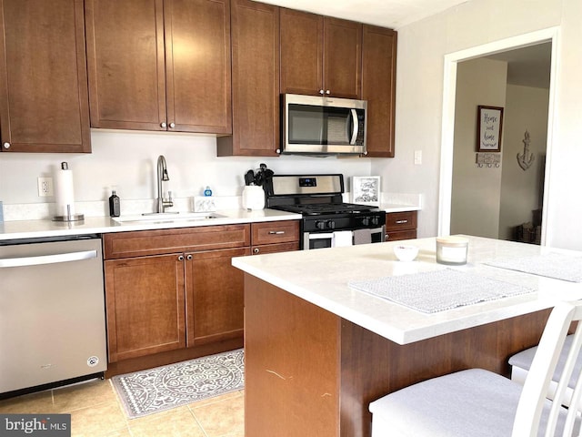 kitchen with a kitchen breakfast bar, stainless steel appliances, light tile patterned floors, and sink