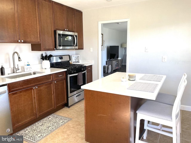 kitchen featuring a kitchen breakfast bar, stainless steel appliances, sink, light tile patterned floors, and a kitchen island