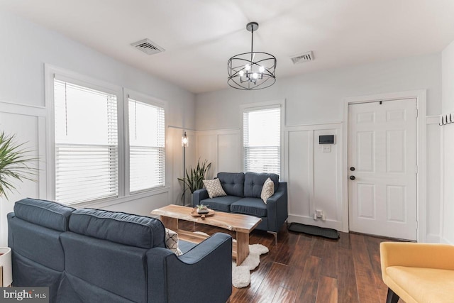 living room with an inviting chandelier, a wealth of natural light, and dark wood-type flooring