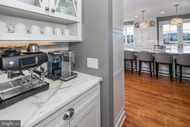 kitchen with backsplash, hardwood / wood-style floors, white cabinets, and pendant lighting