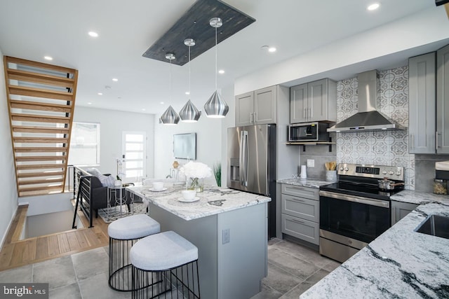 kitchen with light stone counters, stainless steel appliances, gray cabinets, and wall chimney range hood