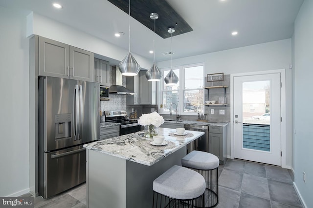 kitchen featuring appliances with stainless steel finishes, a center island, gray cabinetry, and wall chimney range hood