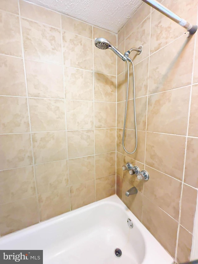 bathroom with a textured ceiling and tiled shower / bath