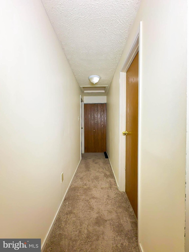 hallway featuring light colored carpet and a textured ceiling