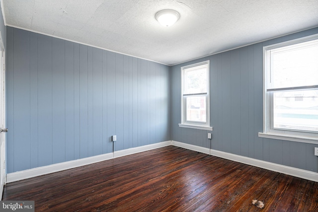 spare room featuring a textured ceiling, dark hardwood / wood-style floors, and wood walls