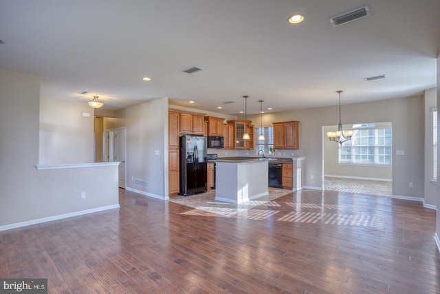 kitchen with dark wood-type flooring, black appliances, a chandelier, a center island, and hanging light fixtures