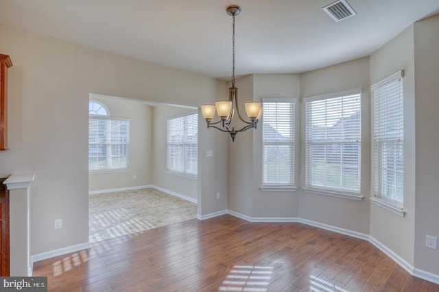 unfurnished dining area featuring plenty of natural light, wood-type flooring, and a notable chandelier