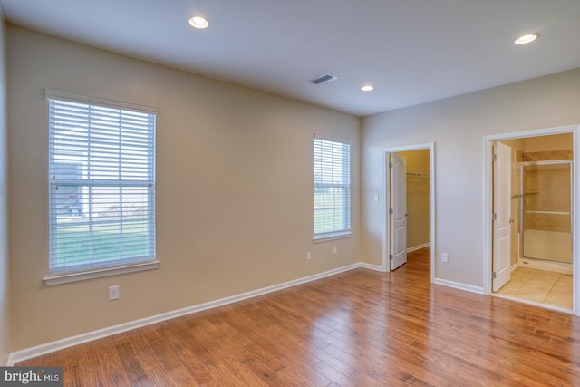 unfurnished bedroom with connected bathroom, a spacious closet, a closet, and light wood-type flooring