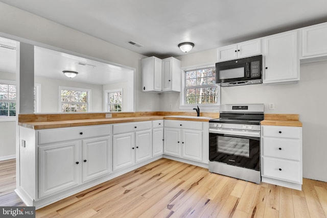 kitchen featuring white cabinets, butcher block countertops, a healthy amount of sunlight, and stainless steel stove