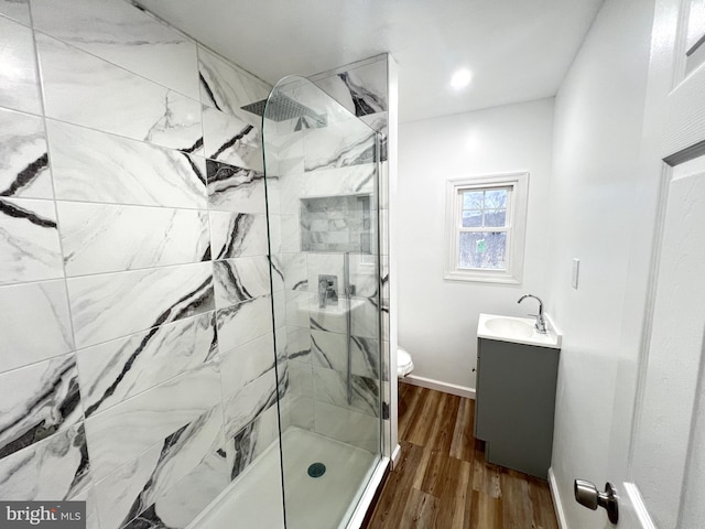 bathroom with hardwood / wood-style floors, vanity, toilet, and tiled shower