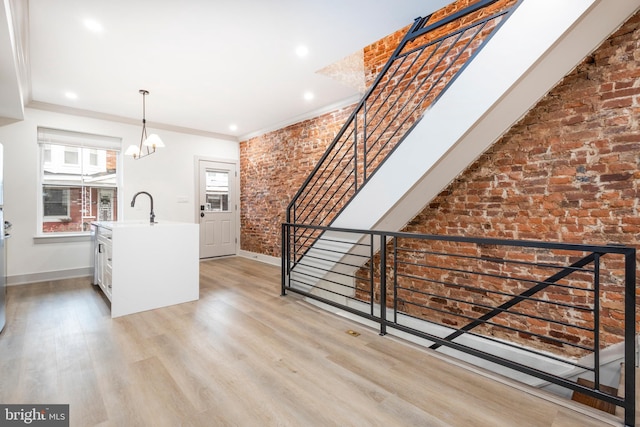 interior space with light wood-type flooring, ornamental molding, brick wall, sink, and a chandelier