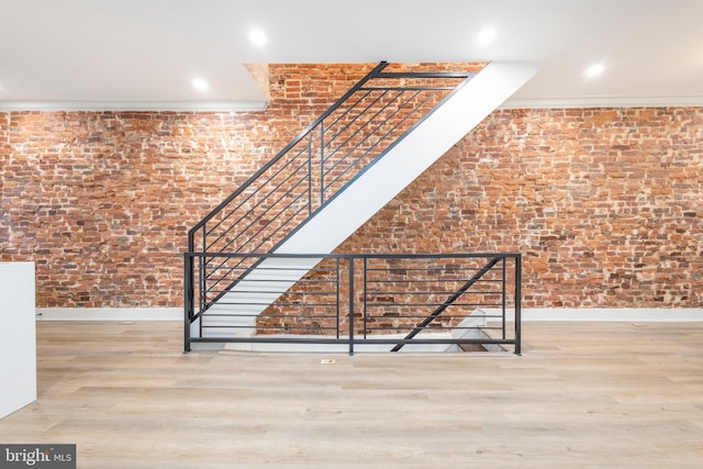 stairs featuring wood-type flooring, brick wall, and ornamental molding