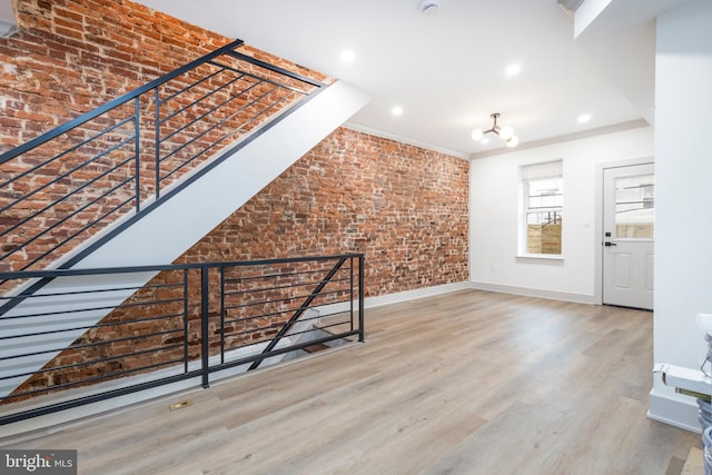 unfurnished living room with wood-type flooring, crown molding, brick wall, and an inviting chandelier