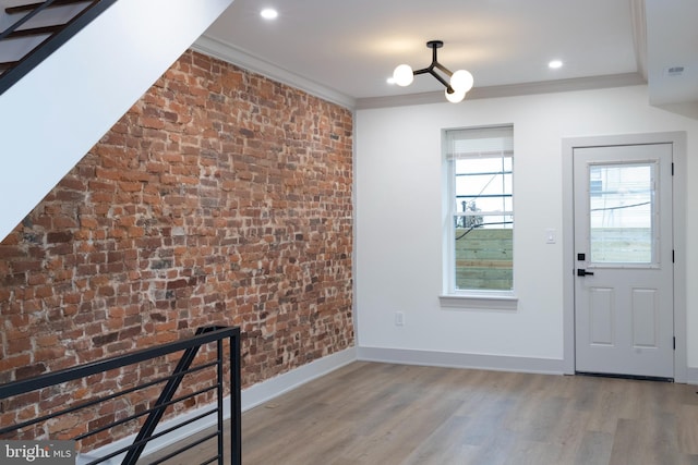 entryway featuring hardwood / wood-style floors, an inviting chandelier, ornamental molding, and brick wall