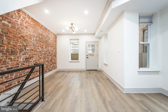 foyer entrance with light hardwood / wood-style floors, an inviting chandelier, crown molding, and brick wall