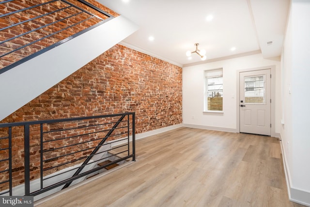 entrance foyer with crown molding, hardwood / wood-style floors, brick wall, and an inviting chandelier