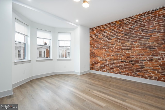 spare room featuring light hardwood / wood-style flooring and brick wall