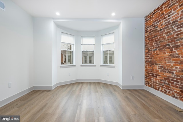 empty room featuring brick wall and light wood-type flooring