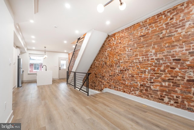 unfurnished living room with sink, light hardwood / wood-style flooring, ornamental molding, and brick wall