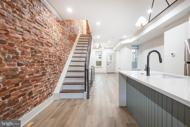 kitchen featuring stainless steel refrigerator, light hardwood / wood-style flooring, brick wall, and sink