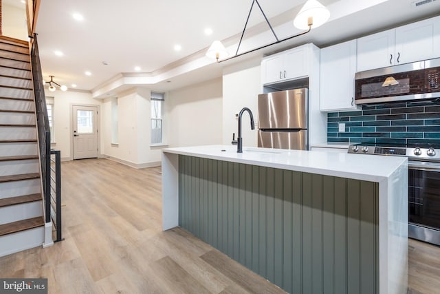 kitchen featuring white cabinetry, tasteful backsplash, a center island with sink, appliances with stainless steel finishes, and light wood-type flooring