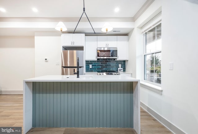 kitchen featuring stainless steel appliances, light hardwood / wood-style flooring, hanging light fixtures, and an island with sink