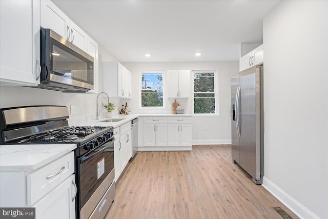 kitchen featuring white cabinetry, sink, stainless steel appliances, light stone counters, and light hardwood / wood-style flooring