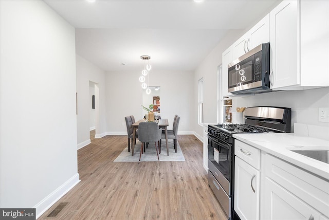 kitchen with light stone countertops, light wood-type flooring, stainless steel appliances, and white cabinetry