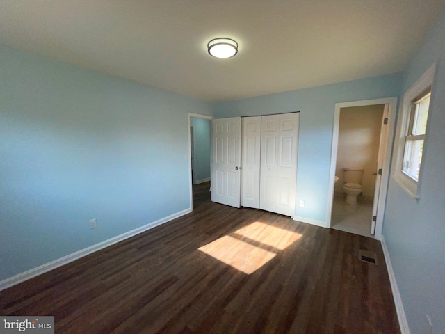 unfurnished bedroom featuring ensuite bath, a closet, and dark wood-type flooring