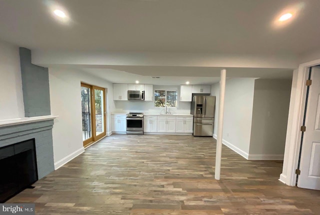 kitchen featuring white cabinetry, sink, wood-type flooring, a fireplace, and appliances with stainless steel finishes