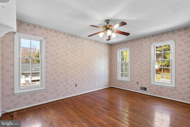 spare room with wallpapered walls, baseboards, visible vents, and wood-type flooring