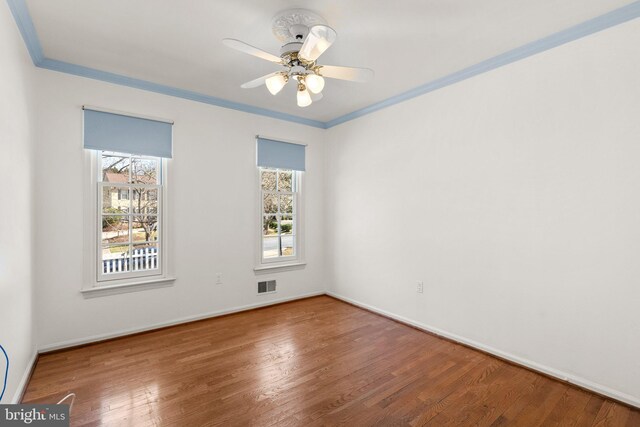 empty room featuring hardwood / wood-style flooring, crown molding, a healthy amount of sunlight, and visible vents