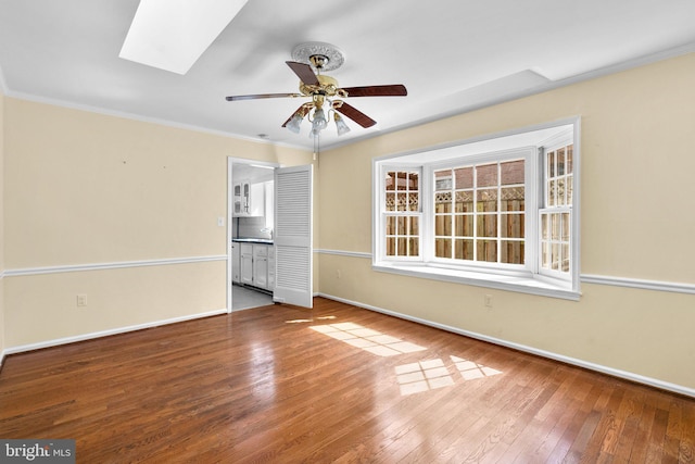 unfurnished room featuring baseboards, a skylight, ceiling fan, hardwood / wood-style flooring, and crown molding