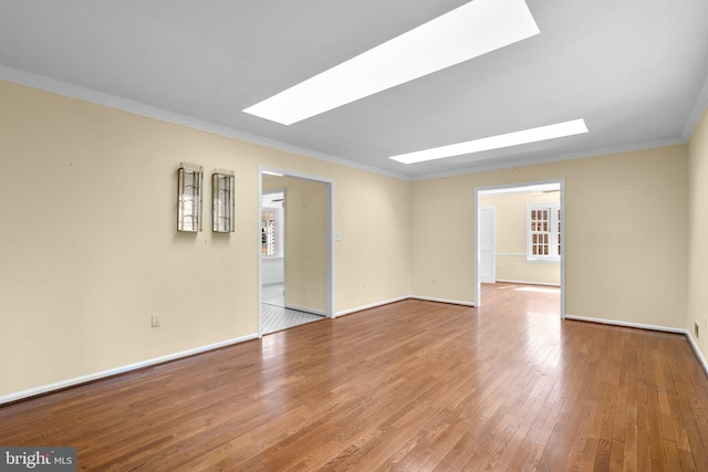 spare room featuring a skylight, crown molding, baseboards, and hardwood / wood-style flooring