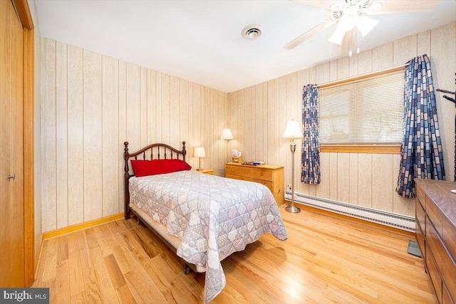 bedroom with ceiling fan, wood walls, wood-type flooring, and a baseboard heating unit