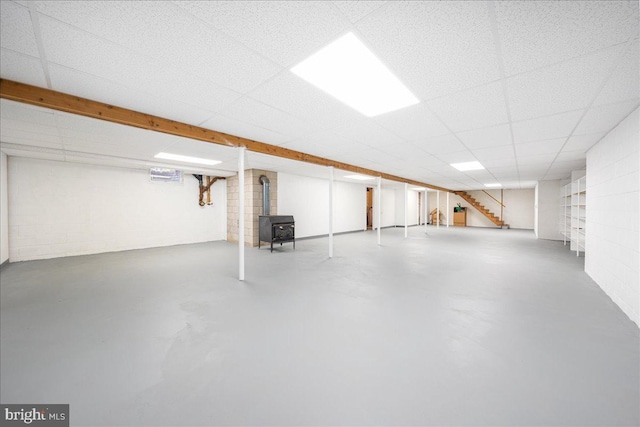 basement featuring a paneled ceiling and a wood stove