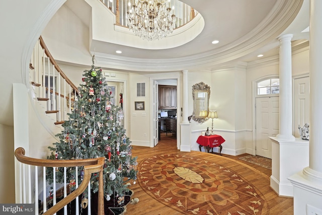 entrance foyer with wood-type flooring, an inviting chandelier, a raised ceiling, and crown molding