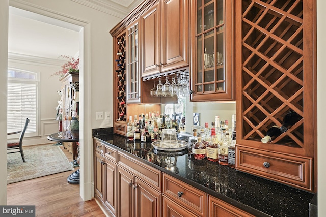 bar with light hardwood / wood-style flooring, ornamental molding, and dark stone countertops