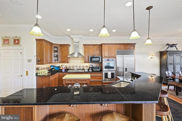 kitchen featuring a kitchen breakfast bar, pendant lighting, stainless steel appliances, and wall chimney range hood