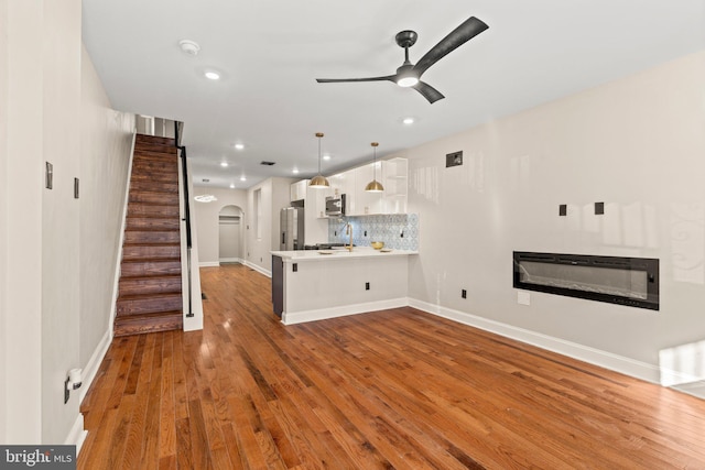 unfurnished living room featuring hardwood / wood-style floors, heating unit, ceiling fan, and sink