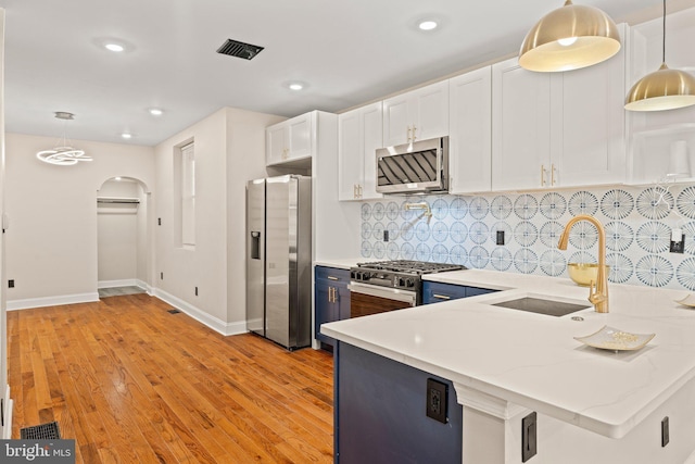 kitchen with hanging light fixtures, white cabinets, stainless steel appliances, and light hardwood / wood-style floors