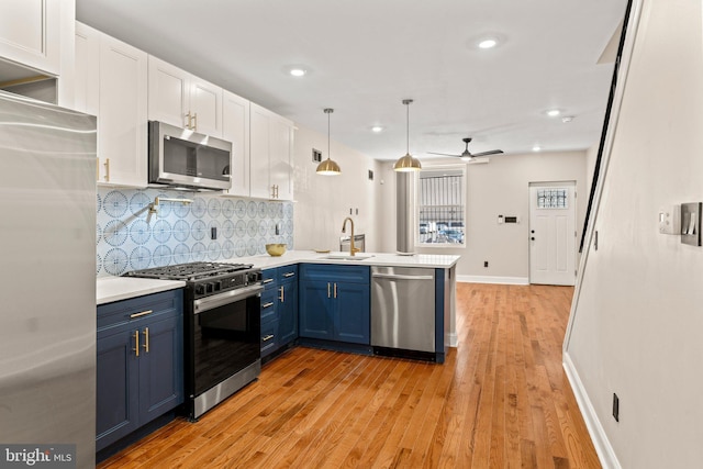 kitchen with pendant lighting, blue cabinets, sink, light hardwood / wood-style flooring, and appliances with stainless steel finishes