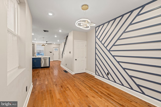 unfurnished living room with ceiling fan with notable chandelier and light wood-type flooring