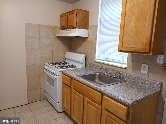 kitchen featuring gas range gas stove, sink, light tile patterned flooring, and tile walls