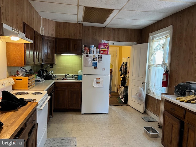 kitchen with a paneled ceiling, decorative backsplash, wood walls, and white appliances