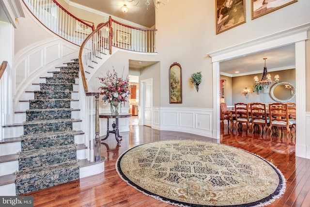 entrance foyer with ornamental molding, wood-type flooring, a high ceiling, and an inviting chandelier