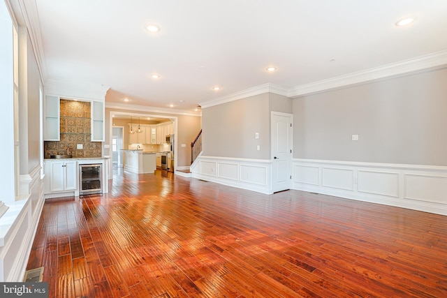 unfurnished living room featuring wood-type flooring, beverage cooler, and crown molding