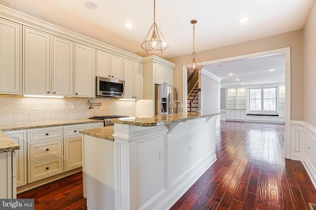 kitchen featuring a kitchen island with sink, decorative light fixtures, light stone countertops, and appliances with stainless steel finishes