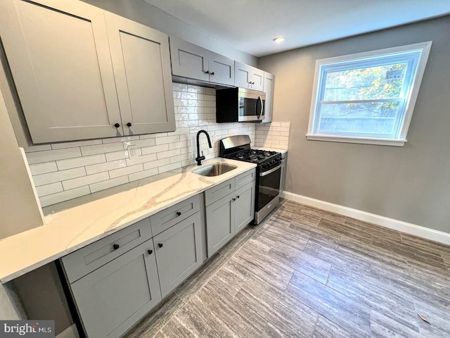 kitchen with sink, gray cabinets, appliances with stainless steel finishes, light stone counters, and decorative backsplash