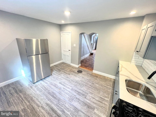 kitchen featuring sink, gray cabinets, light hardwood / wood-style floors, light stone counters, and stainless steel refrigerator